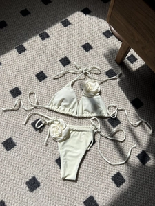 Creamy white bikini set featuring 3D floral accents and side-tie bottom on flat lay view