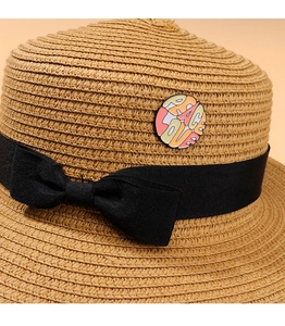 Detail of Peace Love enamel pin on a beige straw hat with black ribbon decoration