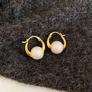 Detailed close-up of gold-plated hoop earrings with round white pearls on dark grey fabric