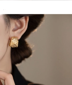 Close-up of golden geometric C-shaped earrings with vintage hammered metal texture on ear