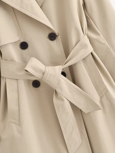 Detail of khaki trench coat featuring double-breasted buttons and tied waist belt