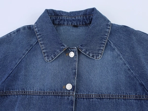 Detailed close-up of blue denim jacket showing orange stitching and silver metal buttons
