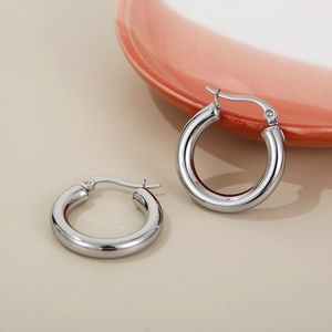Close-up of polished silver stainless steel hoop earrings on a minimalist background