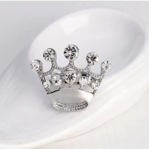 Detailed view of silver crown brooch with sparkling rhinestones on a white surface