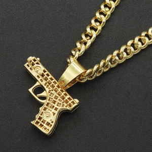 Gros plan d'un pendentif pistolet doré évidé sur une chaîne à mailles cubaines
