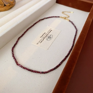 Vue détaillée d'un collier de perles rouge foncé sur plateau en velours beige et carte vintage