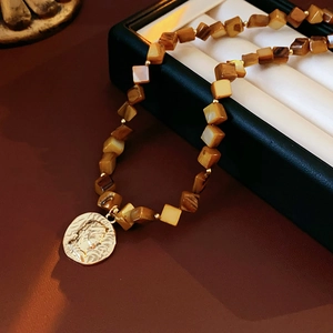 Detail of necklace with brown square beads and golden relief portrait pendant on black box