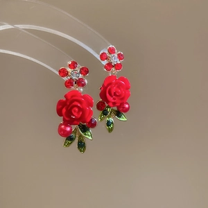Macro detail of red rose earrings featuring rhinestone accents and leaf drop design