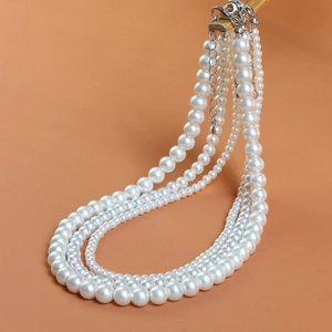 Three-layer white pearl necklace with adjustable silver lobster clasp on warm background