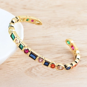 Detail of gold open bracelet with multi-shape rainbow cubic zirconia on a warm desk