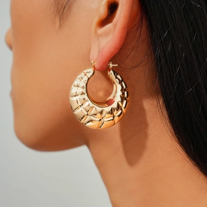 Macro view of gold chunky hoop earrings featuring a quilted geometric metal texture