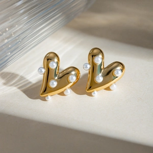 Macro detail of 18k gold heart-shaped earrings with white pearls on a minimalist background