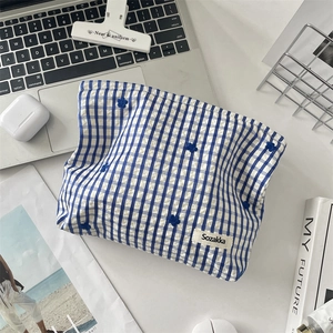 Détail d'une trousse à maquillage à carreaux bleus avec broderie florale et étiquette