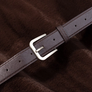 Détail de la ceinture en cuir marron foncé avec boucle argentée sur fond de fausse fourrure