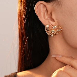 Close-up of golden heart-shaped windmill stud earrings with sparkling rhinestones on model