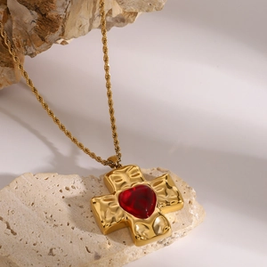 Detailed shot of gold cross pendant with red heart gemstone on textured rock surface