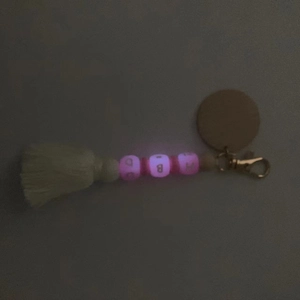 Détail de perles roses lumineuses et pompon blanc sur porte-clés en bois sculpté