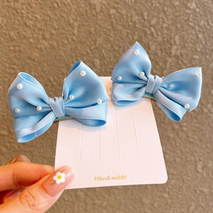 Close-up of sky blue satin hair bows with white pearls on a display card for girls