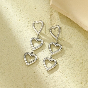 Detailed view of silver triple hollow heart drop earrings on a textured surface