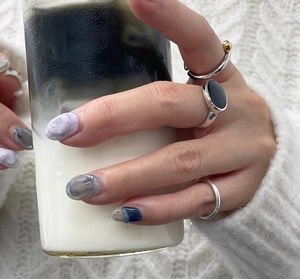 Detail of layered S925 silver rings with black gemstone and gold bead accent on model hand