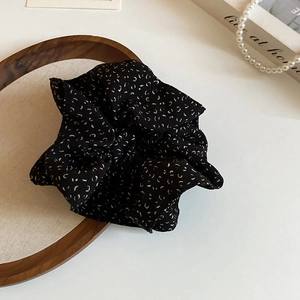Close-up of a black scrunchie with floral print on a wooden tray with a pearl necklace
