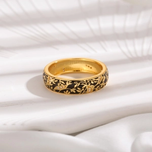 Macro view of gold-plated wide ring with black enamel vines and small crystals