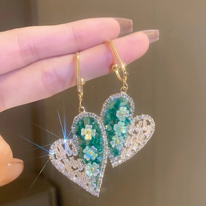 Detailed macro view of heart earrings featuring green stones and clear crystals
