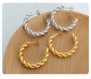 Detail of gold and silver twisted rope hoop earrings on a round wooden tray surface