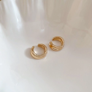 Detailed close-up of a pair of gold geometric C-shaped ear cuffs on a white ceramic plate