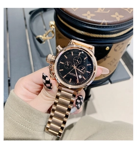 Close-up of rose gold watch with black dial and metal strap worn next to luxury bag