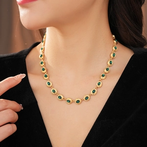 Détail d'un collier vintage doré avec pierres ovales vertes porté par un modèle
