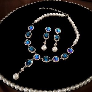 Vintage style jewelry set with blue gemstones and pearls on black velvet background