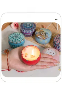 Hand holding a lit scented candle in a floral mosaic tin with dried flower petals
