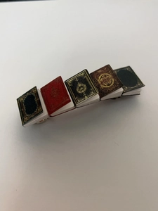 Close-up of five miniature vintage books arranged on a metallic hair clip accessory