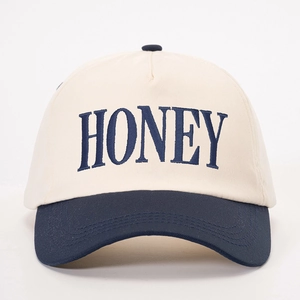 Detailed close-up of HONEY embroidery on a two-tone cotton baseball cap with blue brim