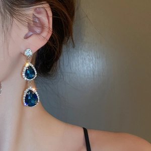 Dettaglio di un orecchino con gemma blu a goccia e piccoli cristalli indossato da modella