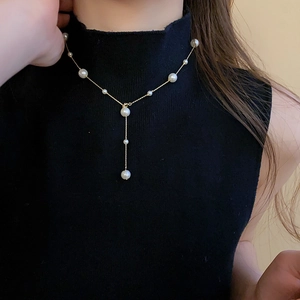 Detailed close-up of a French style Y-shaped gold pearl necklace on a black sweater