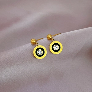 Macro shot of gold Roman numeral stud earrings with a central zircon on purple fabric