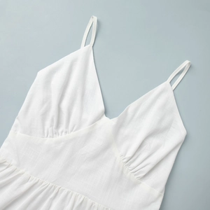 Detail of white cotton V-neck dress showing fine straps and pleated waist texture