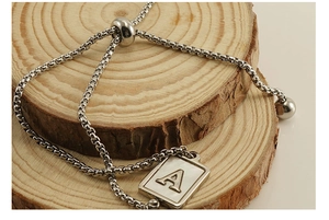 Detail eines silbernen Buchstaben-A-Armbands auf Holz mit verstellbarem Schiebeverschluss