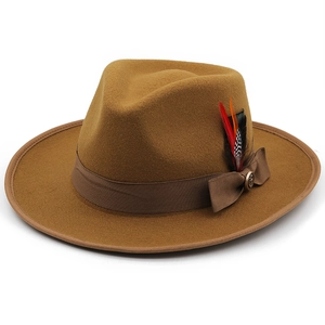 Detail view of camel wool fedora hat with brown ribbon, metal badge and colorful feathers