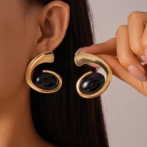 Detail of gold-tone geometric C-shape earrings with a large oval black resin gemstone