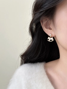 Close-up of golden rocking horse earrings with white pearl detail on a female model