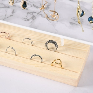 Detail of wooden jewelry display stand with rings and pearl earrings on marble surface