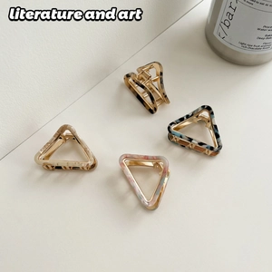 Detail view of four triangular acetate hair claws with diverse marble textures and gold metal base