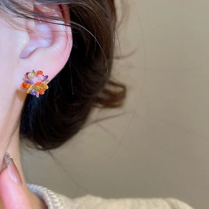 Close-up of colorful crystal flower stud earrings worn by a model in soft light