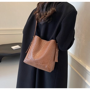 Detail of a brown woven bucket bag with textured faux leather on a female model