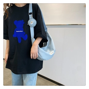 Détail d'un t-shirt noir oversize avec imprimé ours bleu et un sac à bandoulière