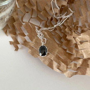 Detailed macro view of black faceted gemstone pendant with silver prong setting and fine chain