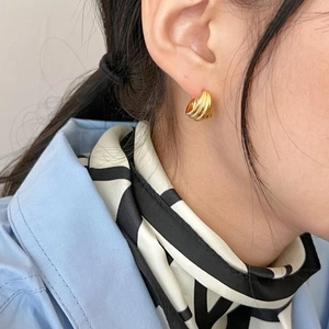 Detail of golden ribbed hoop earrings on model with silk scarf for a French chic look